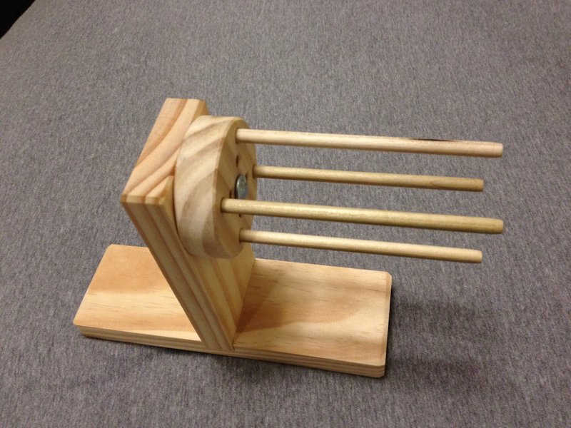 Wooden monkey-fist tying jig with four dowels on a grey carpet
