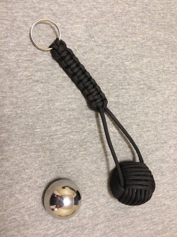 Black paracord monkey fist next to a 1 inch steel bearing and a split ring